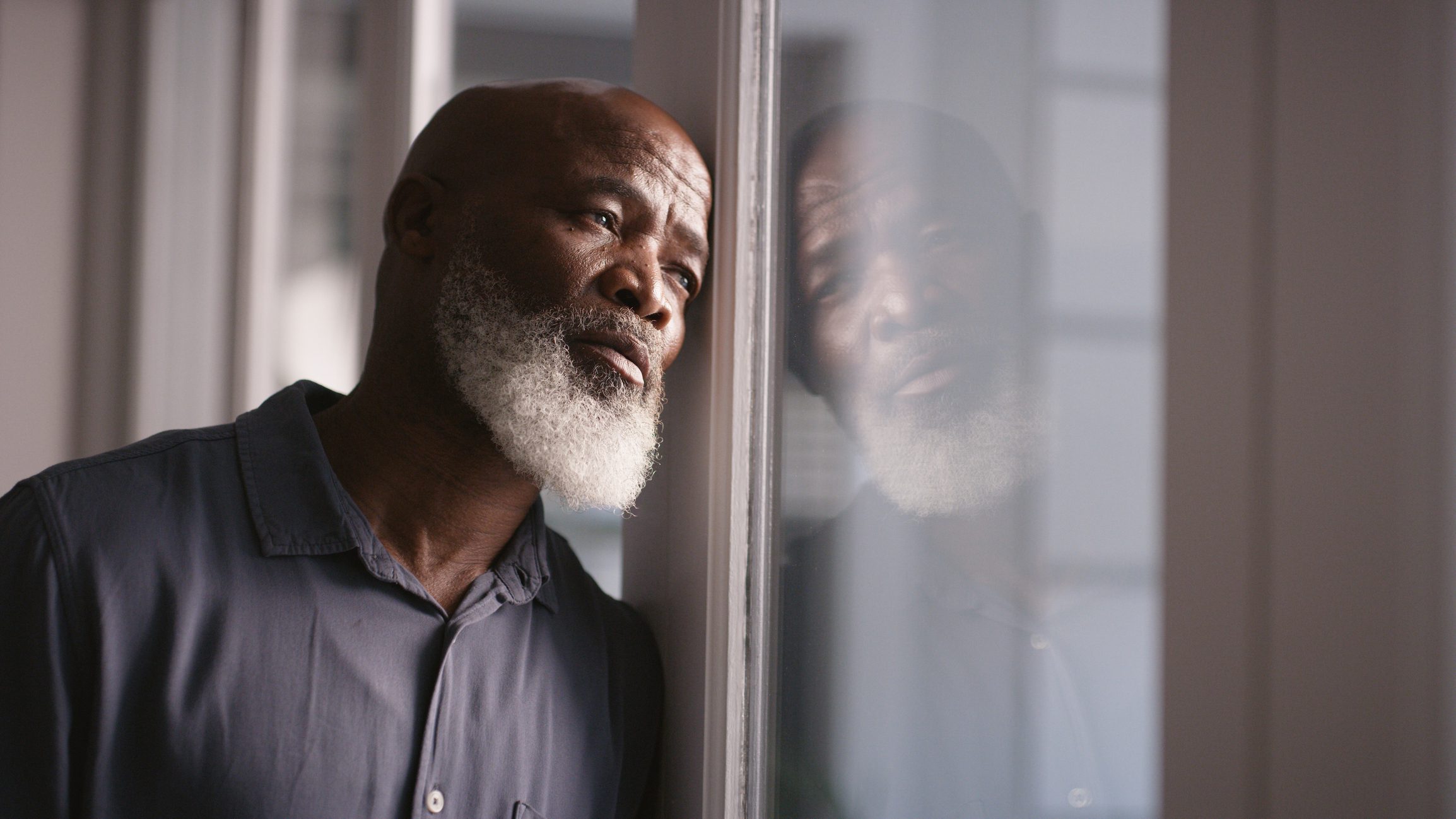 Grieving man looks longingly out a window on a cloudy day.